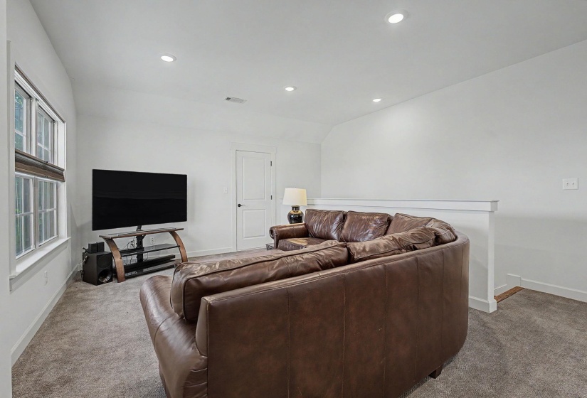 Carpeted entertainment area featuring white walls, recessed lighting, a window with horizontal blinds, and a white interior door