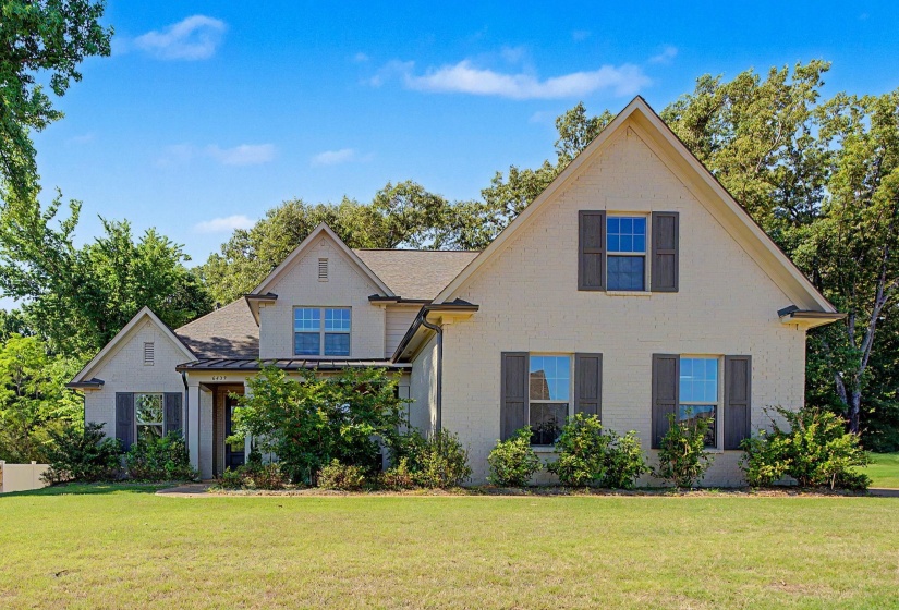 Traditional-style residence featuring a pale brick exterior with dark shutters, multiple gables, a covered entry, and established perimeter landscaping