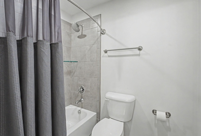 Bathroom featuring a white bathtub, tiled shower surround, wall-mounted glass shelves, rain shower head, and chrome fixtures