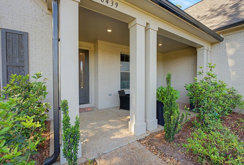 Covered front porch featuring a dark entry door with decorative glass, brick exterior, and decorative shutters