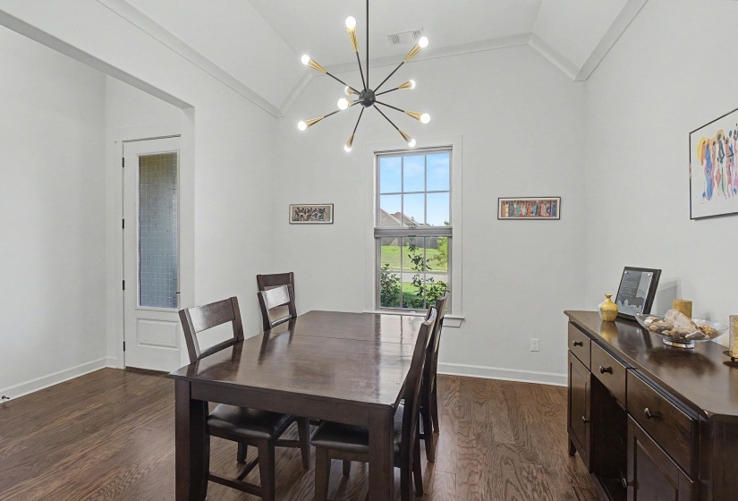 Formal dining area featuring a vaulted ceiling with exposed beams, a modern sputnik chandelier, wood-finish flooring, and a window with exterior views