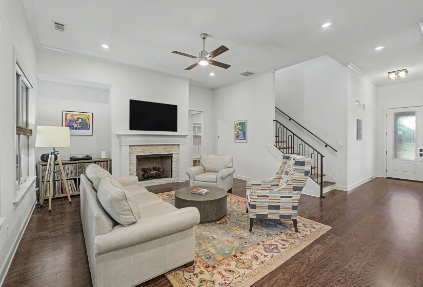 Living area featuring dark wood-finish flooring, a fireplace with a stone surround and white mantel, a ceiling fan, and recessed lighting