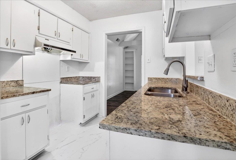 Kitchen featuring white cabinetry, light-toned stone countertops, a stainless steel sink with a gooseneck faucet, and white tile flooring