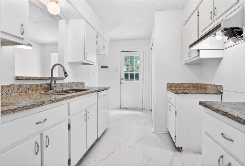 Kitchen featuring white cabinetry, granite countertops, a stainless steel sink with a gooseneck faucet, a built-in dishwasher, and white tile flooring