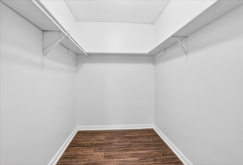 Interior closet featuring wrap-around shelving with hanging rods and wood-finish flooring