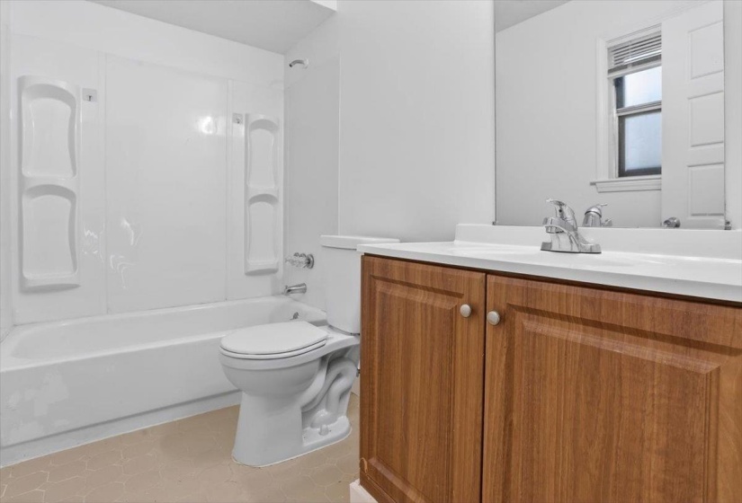Full bathroom featuring a white tub and shower surround, a toilet, a vanity with wood-finish cabinetry, a white countertop, and a chrome faucet
