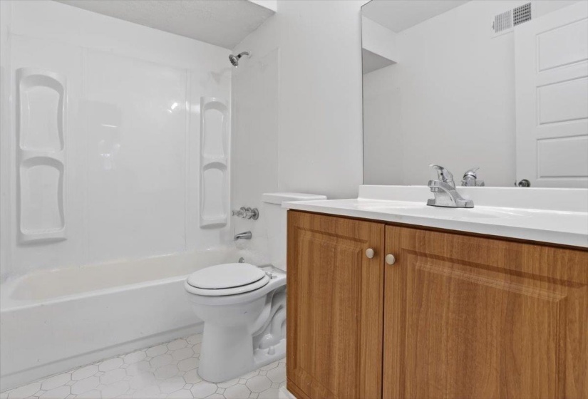 Bathroom featuring a white tub/shower combination, white toilet, and wood-finish vanity with a white countertop and chrome faucet