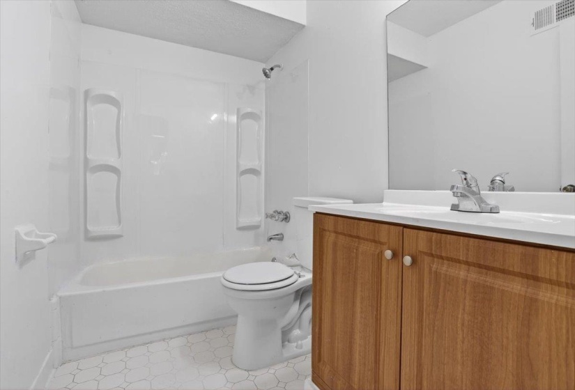 Bathroom featuring a white bathtub and shower surround, a toilet, a wood-finish vanity with an integrated sink, and a large wall mirror