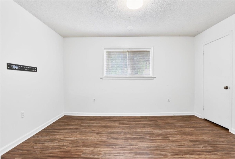Room featuring wood-finish flooring, white baseboards, a single window, and a wall-mounted light fixture