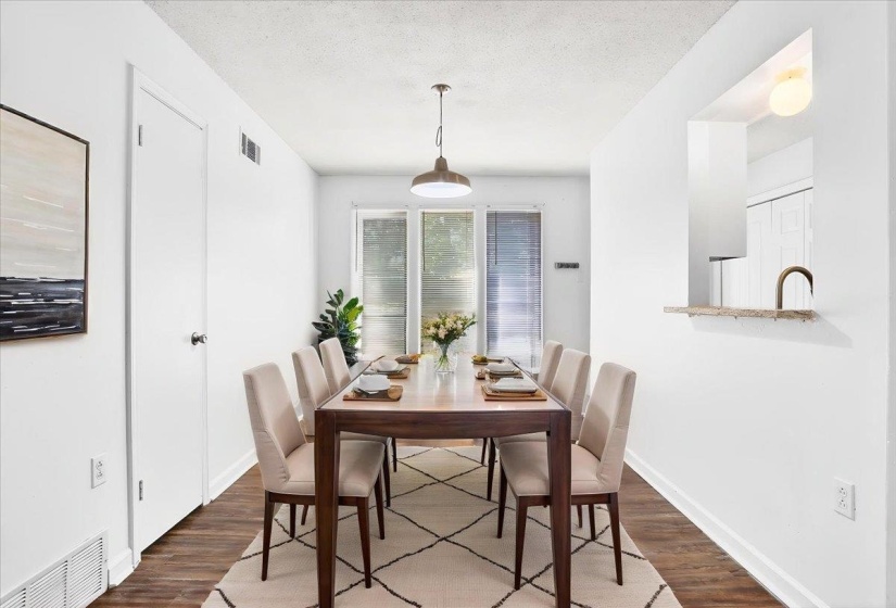 Dining area featuring wood-finish flooring, white walls, and a contemporary pendant light fixture (staged)