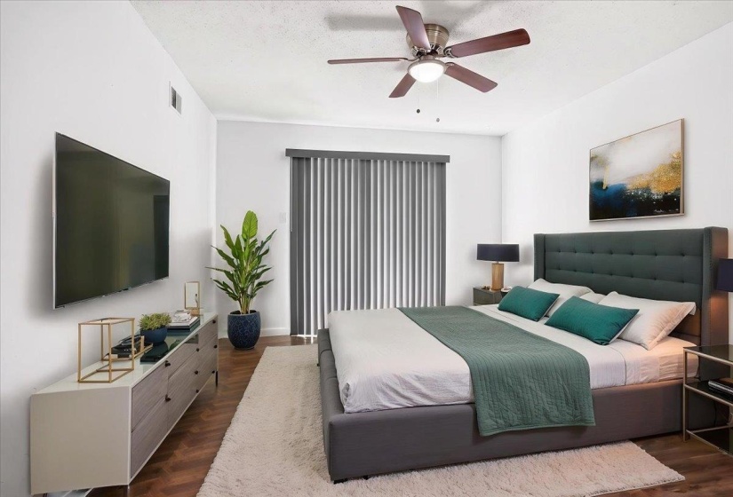 Bedroom featuring wood-finish flooring, a ceiling fan with integrated lighting, and a sliding glass door with vertical blinds (staged)
