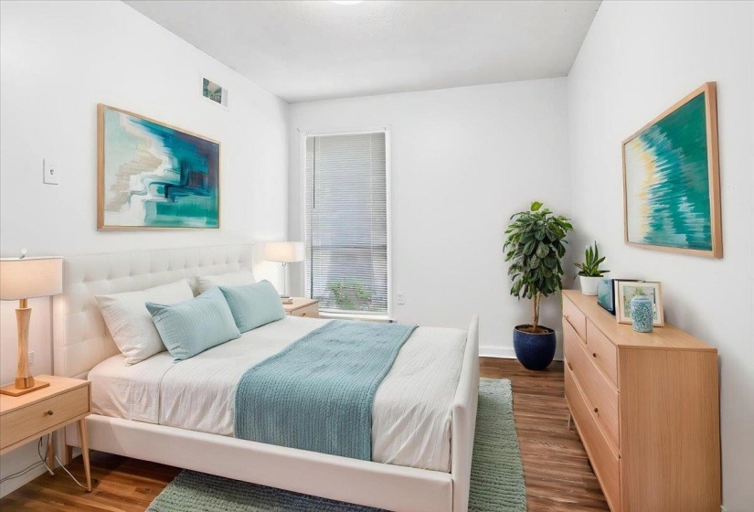 Bright bedroom featuring white walls and wood-finish flooring (staged)