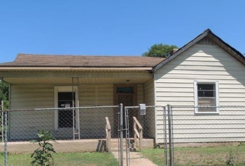 Single-story residence featuring light-colored siding, a covered front porch, and a chain-link fence
