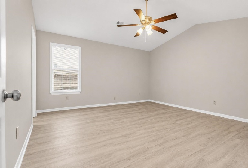 Spacious room featuring vaulted ceilings, wood-finish flooring, a window providing natural illumination, a ceiling fan with integrated lighting, and neutral wall tones