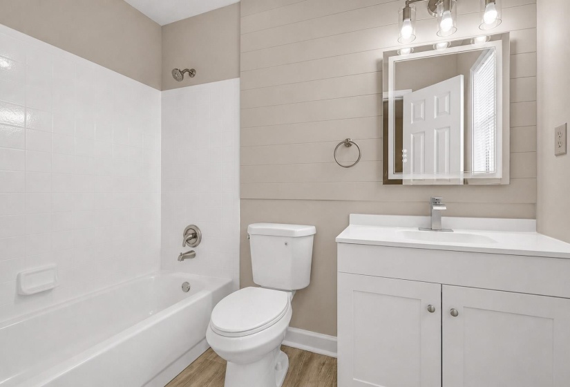 Bathroom featuring a white subway tile tub surround, chrome fixtures, a modern vanity with a white countertop, and plank-style accent wall