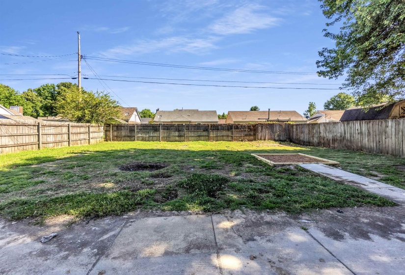 Fenced backyard featuring a concrete patio, a concrete pathway, and a raised garden bed