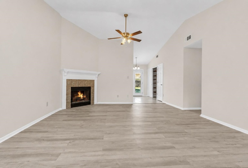Vaulted ceiling living space featuring wood-finish flooring, a corner fireplace with a tiled surround and white mantel, and a ceiling fan with integrated lighting