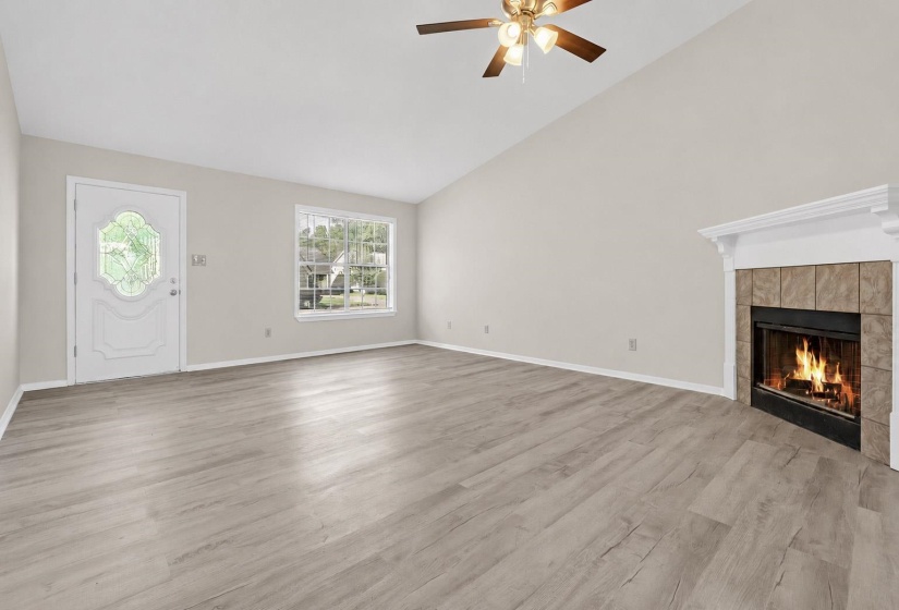 Spacious living area featuring high vaulted ceilings, light wood-finish flooring, a decorative fireplace with a mantel, and a ceiling fan