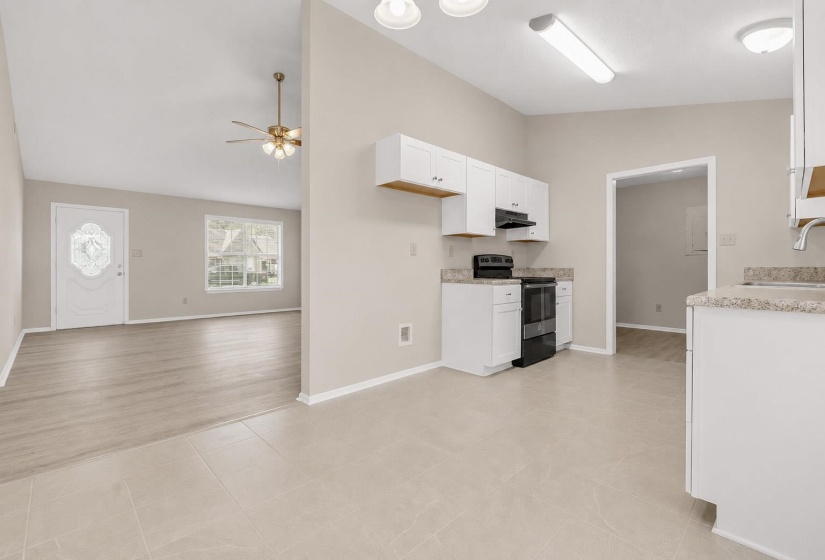 Kitchen area featuring tile flooring, white cabinetry, integrated black range with hood, and stone-finish countertops