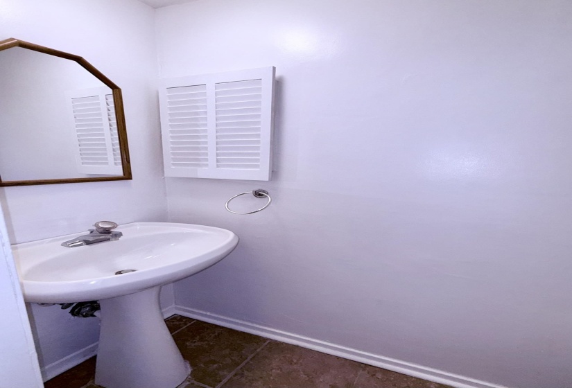 Pedestal sink with chrome faucet, octagonal mirror, white louvered wall panel, and tile flooring
