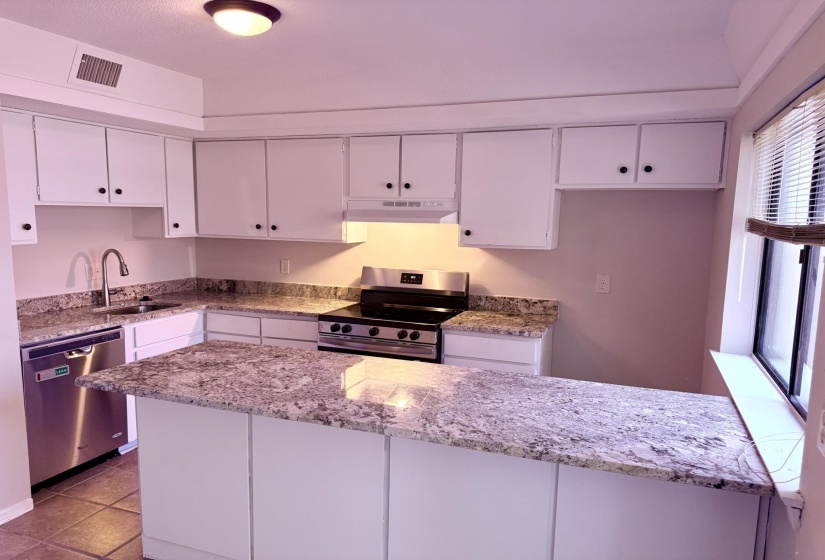 Well-appointed kitchen featuring a peninsula island with stone countertops, white cabinetry, stainless steel appliances, and a built-in sink with a gooseneck faucet