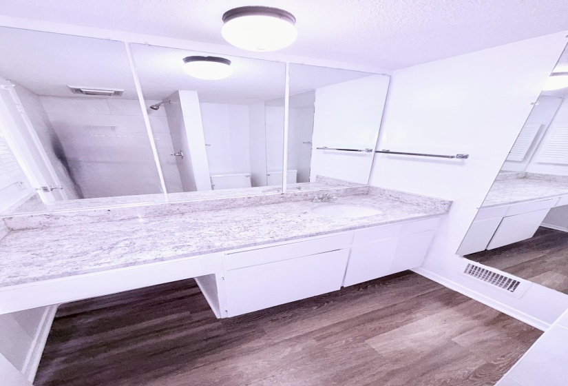 Bathroom featuring a broad vanity with a speckled countertop, integrated sink, and white cabinetry