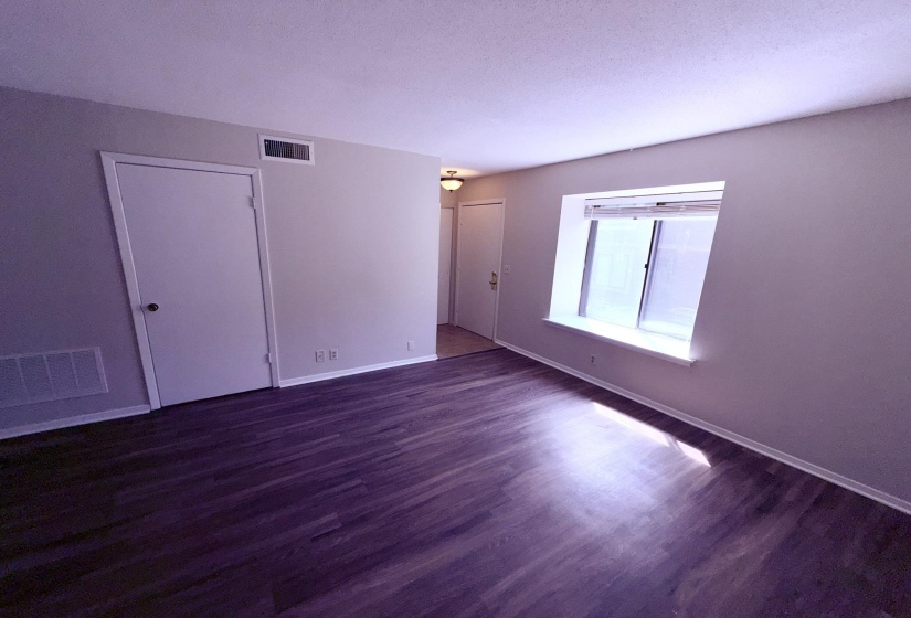 Open living area featuring wood-finish flooring, a large window with blinds, and light-toned wall paint