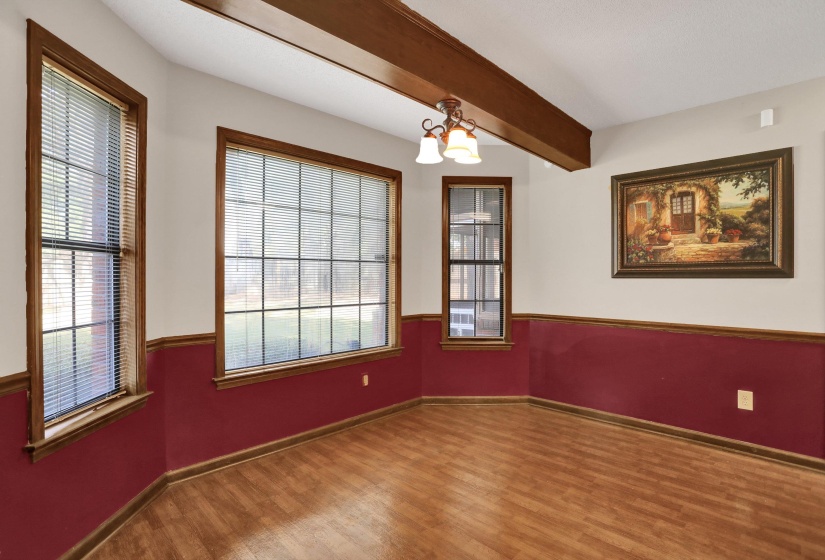 Room featuring wood-finish flooring, exposed ceiling beams, and multiple windows with wood trim