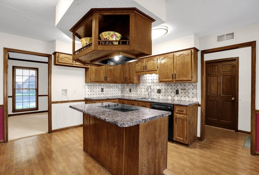 Kitchen featuring wood-finish flooring, oak cabinetry, a center island with a built-in cooktop, and a patterned tile backsplash