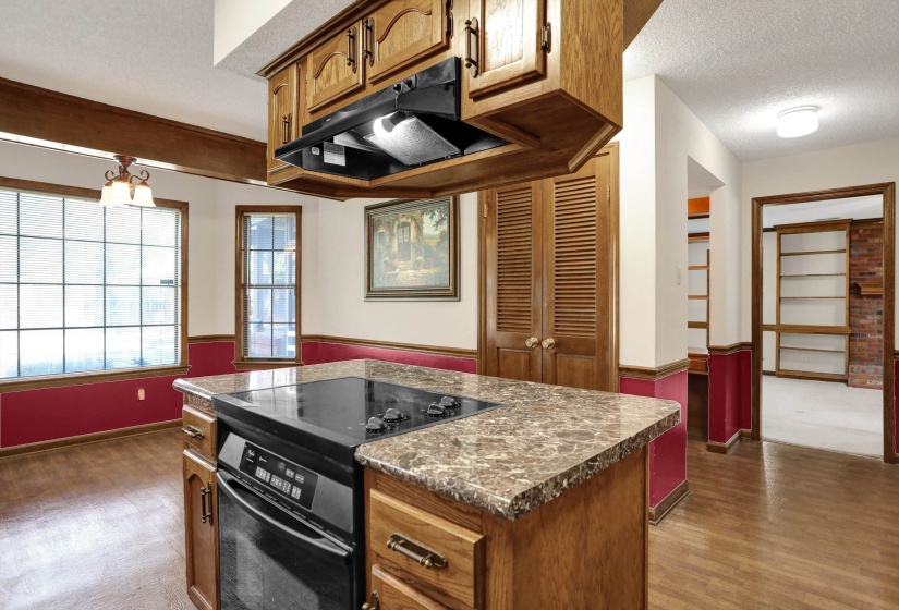 Kitchen island with a built-in electric cooktop, light-toned stone-finish countertop, and wood cabinetry