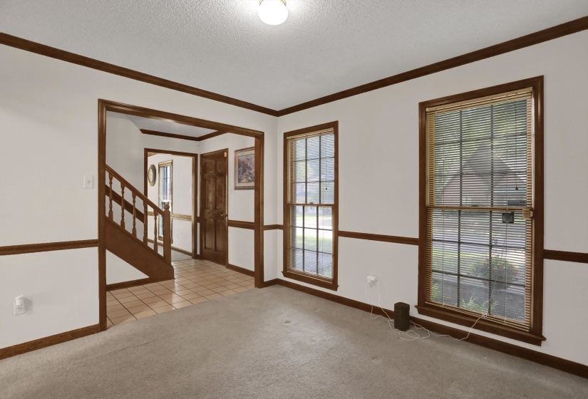 Carpeted interior space featuring white walls with wood trim, an arched entryway, and two double-hung windows with blinds