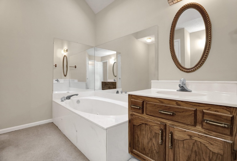 Bathroom featuring a soaking tub with integrated deck, full-wall vanity mirror, a wood-finish vanity with a single basin, an oval framed mirror, and vaulted ceilings