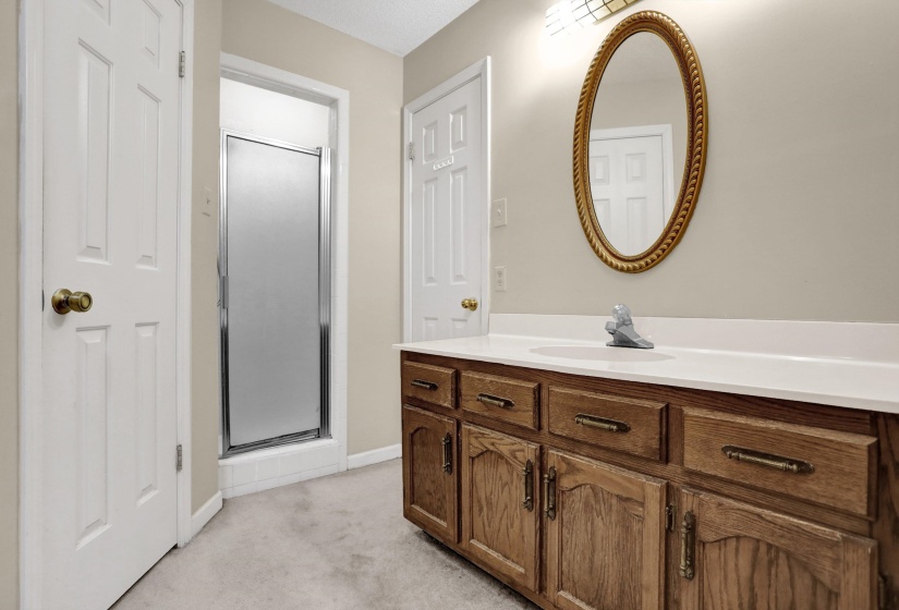 Bathroom featuring a wood-finish vanity with a white countertop, an oval mirror with a decorative frame, and a shower enclosure with a frosted glass door
