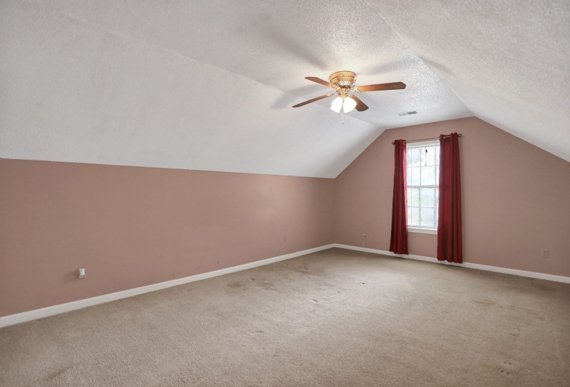Spacious room featuring sloped ceilings, wall-to-wall carpeting, and a window with red drapes