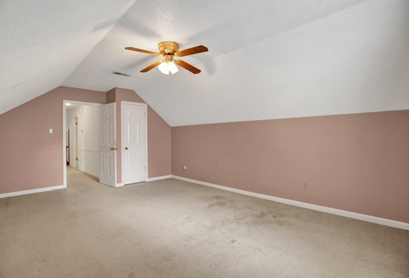 Spacious room featuring sloped ceilings, a ceiling fan with integrated lighting, and neutral carpeting