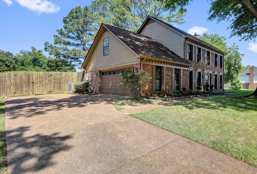 Brick and siding exterior featuring a two-car garage, dark shutters, and a gravel driveway