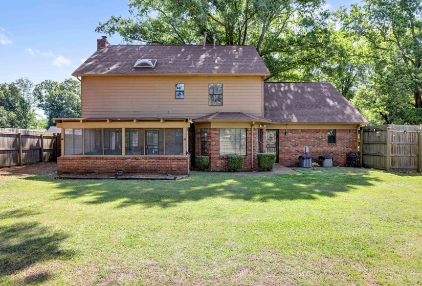 Expansive backyard with a manicured lawn, brick and siding exterior, screened-in porch, privacy fencing, and mature trees