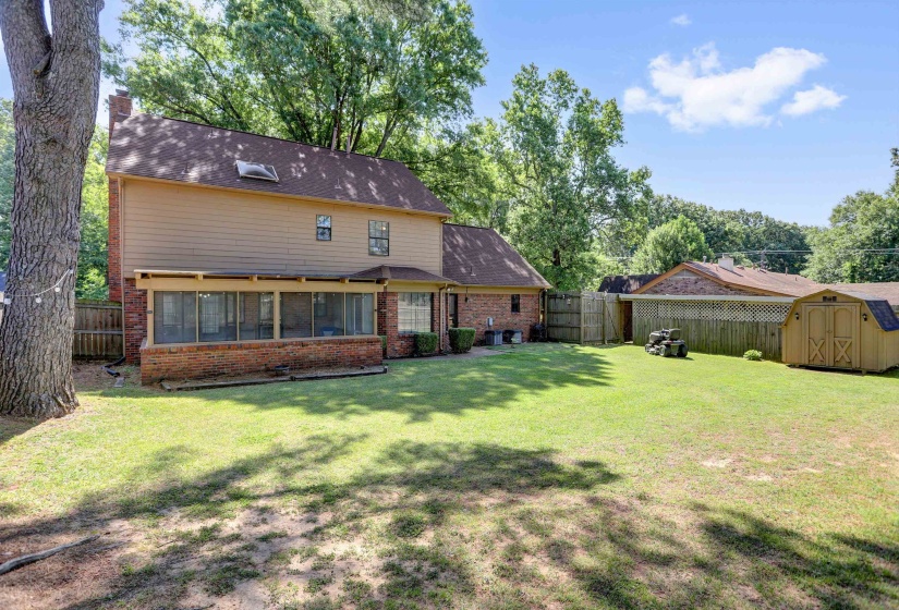 Expansive green lawn featuring a screened porch, privacy fencing, and mature trees