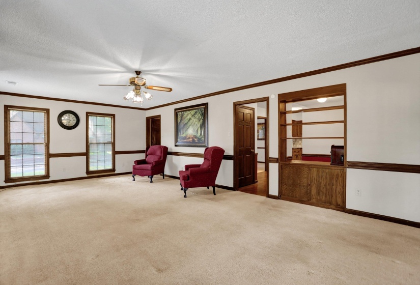 Spacious room featuring carpeting, multiple windows with grid detailing, a ceiling fan with integrated lighting, and dark wood trim