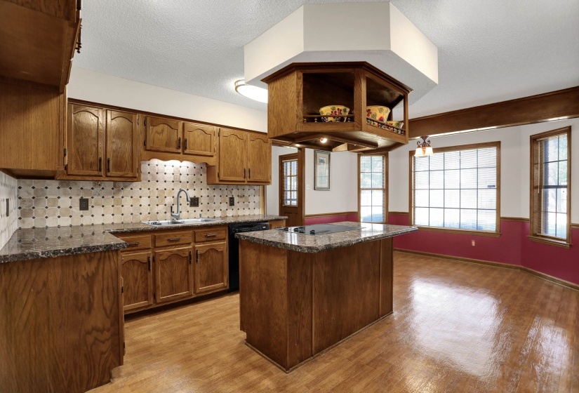 Kitchen featuring wood cabinetry, an island with cooktop, granite-style countertops, mosaic tile backsplash, and wood-finish flooring