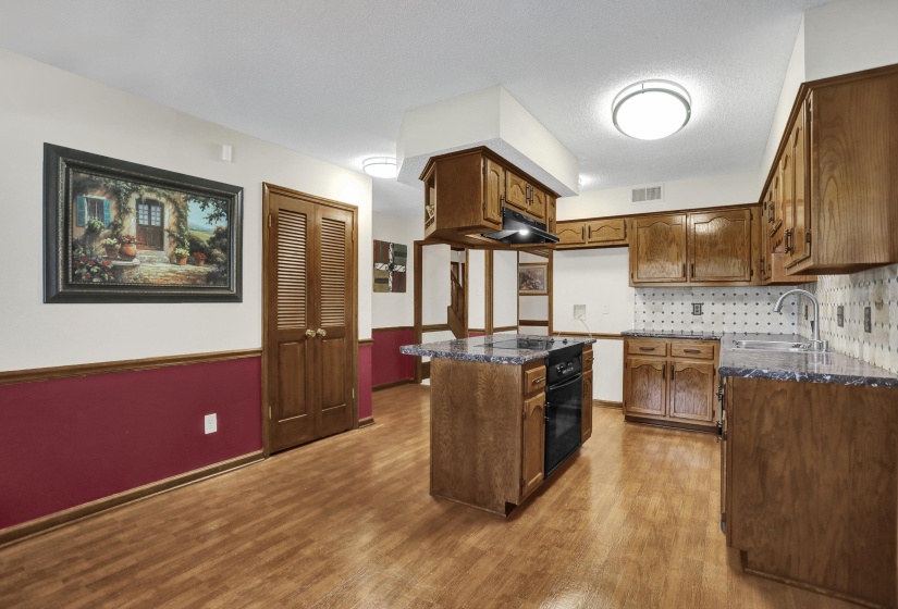 Kitchen featuring wood-finish flooring, wood cabinetry, granite countertops, and a tile backsplash