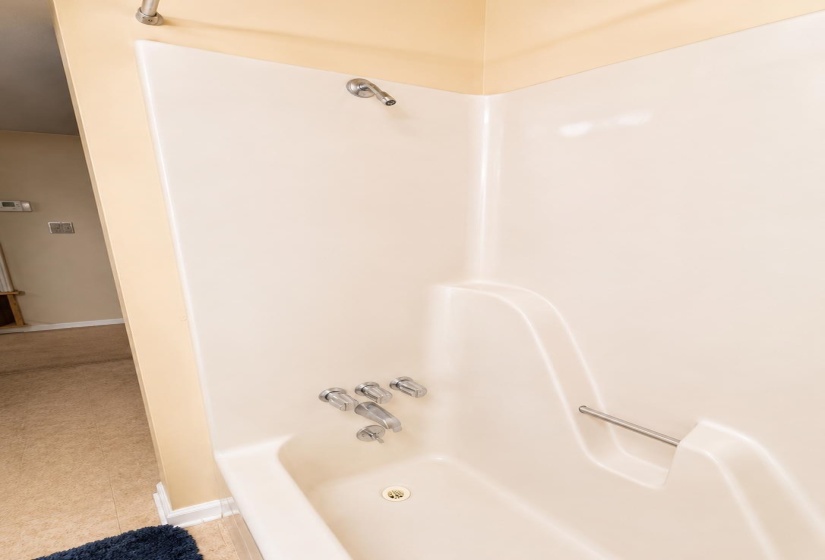 Bathtub and shower combination featuring a built-in grab bar and chrome fixtures AI-Enhanced Photo — May Not Reflect Exact Current Condition