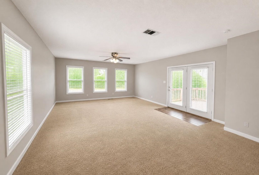 Spacious interior featuring neutral carpeting, light gray walls, and multiple windows with blinds AI-Enhanced Photo — May Not Reflect Exact Current Condition