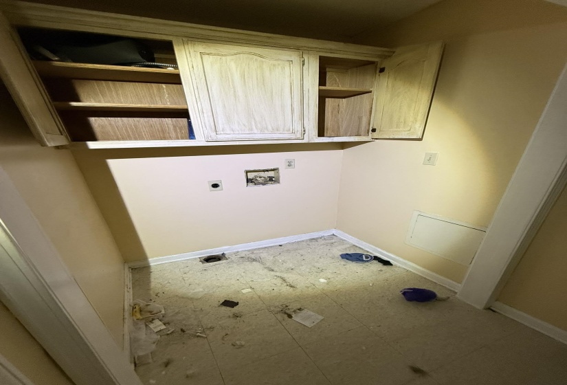 Utility space featuring overhead cabinetry with shelving, wall-mounted electrical outlets, and plumbing hookups