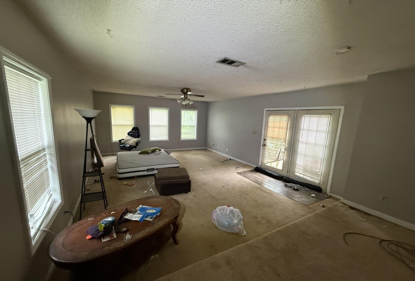Spacious room featuring multiple windows, a ceiling fan with light fixture, and double glass-paneled doors with external access