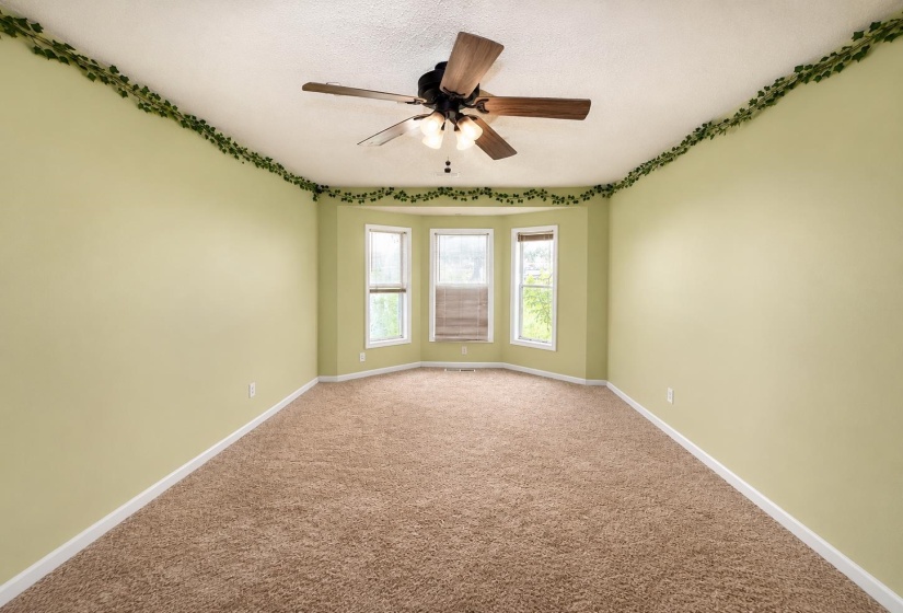 Room featuring a bay window, ceiling fan with light fixture, light green walls, and carpet flooring AI-Enhanced Photo — May Not Reflect Exact Current Condition
