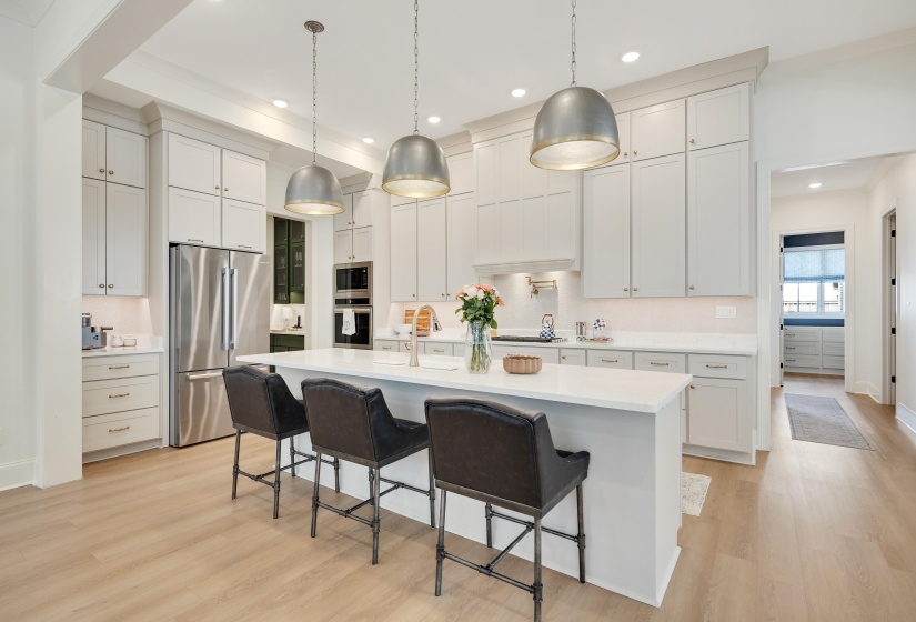 Spacious kitchen featuring a large central island with seating, stainless steel appliances, extensive white cabinetry, light wood-finish flooring, and recessed ceiling lights