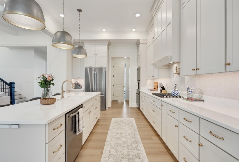 Gourmet kitchen featuring a large central island with integrated sink, stainless steel appliances, extensive white cabinetry, light countertops, and wood-finish flooring