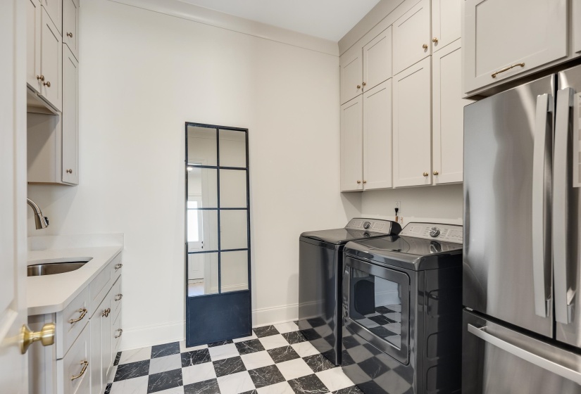 Utility room featuring a checkerboard floor, built-in cabinetry, stainless steel sink, and a multi-paneled interior door