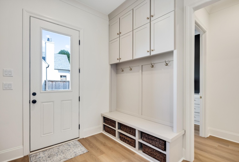 Built-in mudroom cabinetry featuring a seating bench with integrated storage cubbies, upper cabinets with gold-tone hardware, and wall-mounted coat hooks